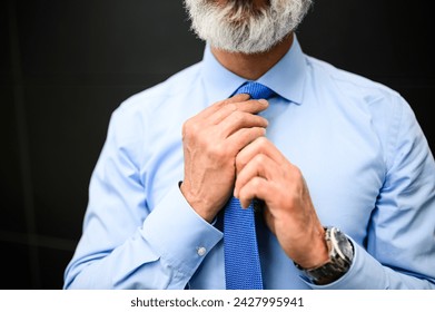 Professional caucasian businessman adjusting his elegant blue necktie and grooming for a job interview in modern corporate attire, with a close-up detail of his hands and wristwatch - Powered by Shutterstock