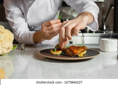 professional caucasian chef-cook decorate dish in the kitchen. man in white apron makes the finishing touch on the dish. culinary, food, restaurant, gourmet concept