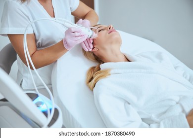 Professional Caucasian dermatologist conducting a microneedling procedure on her young patient using a modern beauty device
