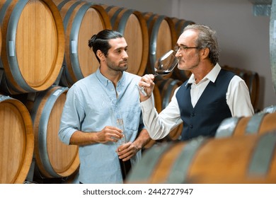 Professional Caucasian man sommelier tasting and sniffing red wine in wooden barrel at traditional wine cellar. Winery, brewery, liquor shop, wine factory manufacturing industry and winemaker concept. - Powered by Shutterstock