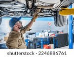 Professional Caucasian Mechanic Standing Under the Vehicle Lifted on Car Lift Checking the Condition of Catalytic Converter. Automotive Theme.