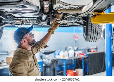 Professional Caucasian Mechanic Standing Under the Vehicle Lifted on Car Lift Checking the Condition of Catalytic Converter. Automotive Theme. - Powered by Shutterstock