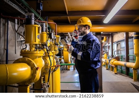 Professional caucasian refinery worker in safety equipment checking gas pipeline installation and pressure.