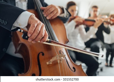 Professional cello player's hands close up, he is performing with string section of the symphony orchestra