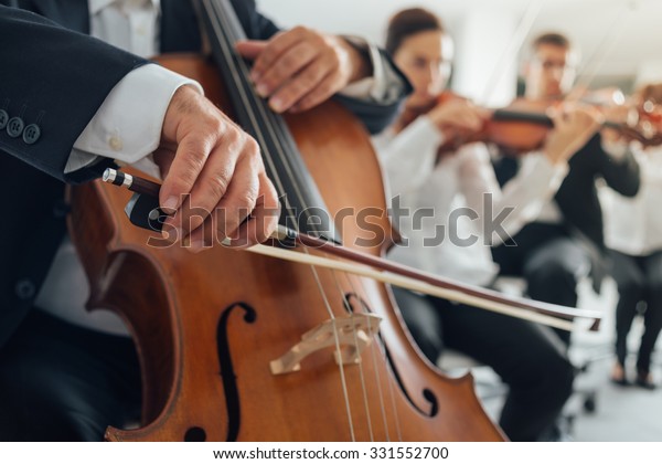 Professional cello player\'s\
hands close up, he is performing with string section of the\
symphony orchestra