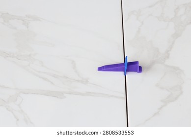Professional ceramic tile installation. The process of leveling white marble tiles using a plastic wedge and clip. Tile leveling system. Using plastic clamps to control the inter-tile seam and plane. Repair