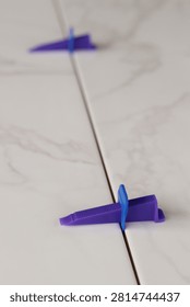 Professional ceramic tile installation. The process of leveling white marble tiles using a plastic wedge and clip. Tile leveling system. Using plastic clamps to control the inter-tile seam and plane. Repair