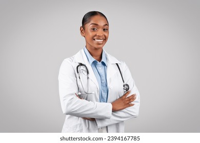 Professional cheerful black doctor smiling at camera, with arms crossed, in white coat and stethoscope on grey background, studio. Medical health care, work and therapist help - Powered by Shutterstock