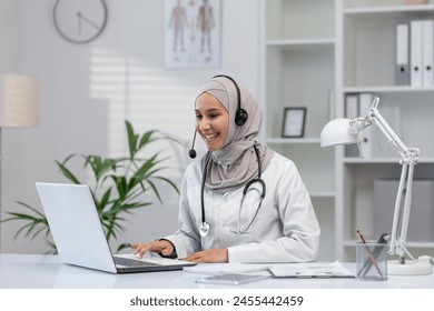 A professional and cheerful female doctor in a hijab provides online consultations from her well-organized office, using a laptop and headset. - Powered by Shutterstock