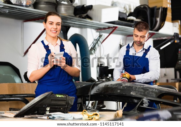 Professional cheerful  smiling\
female mechanic recording list of works on car repair in auto\
repair shop