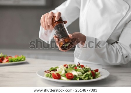 Professional chef adding pepper to delicious salad at white marble table in kitchen, closeup