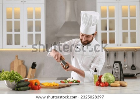 Professional chef adding pepper into delicious salad at marble table in kitchen
