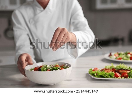 Professional chef adding salt to delicious salad at white marble table in kitchen, closeup
