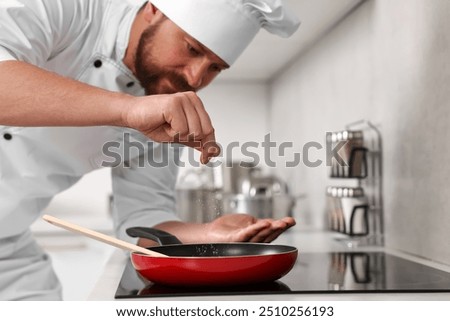 Professional chef adding salt into frying pan in kitchen