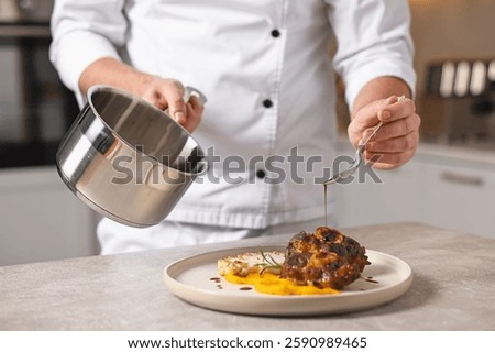 Professional chef adding sauce to delicious dish at table indoors, closeup