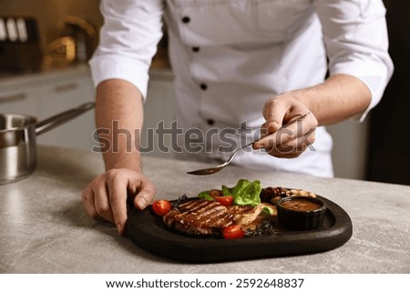 Professional chef adding sauce to delicious dish at table indoors, closeup