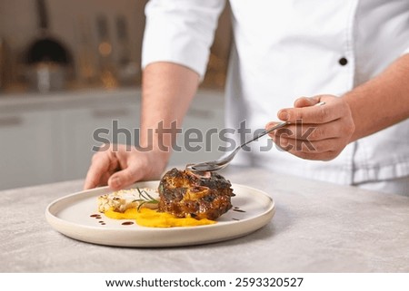 Professional chef adding sauce to delicious dish at table indoors, closeup