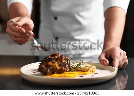 Professional chef adding sauce to delicious dish at table indoors, closeup