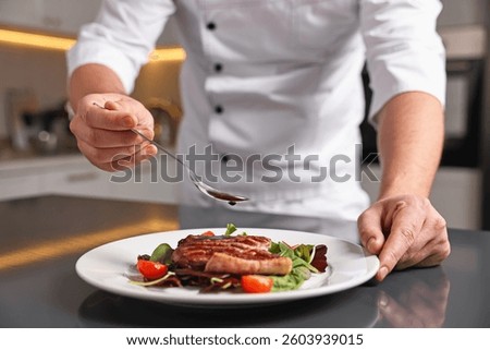 Professional chef adding sauce to delicious dish at table indoors, closeup