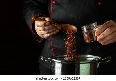A professional chef adds dry red seasonings to a pot of boiling food. Retsoran kitchen cooking concept with advertising space on black background. - Shutterstock ID 2239632387