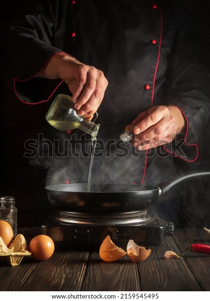 Professional chef adds sweet oil while cooking\
eggs in pan. Work environment on kitchen table. Menu idea for a\
restaurant or\
hotel.