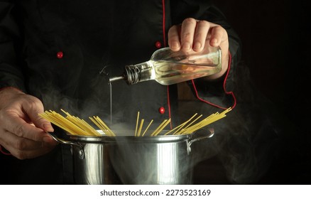 Professional chef adds vegetable oil to a boiling pot of spaghetti. The idea of a delicious national Italian dish. Free space for recipe or menu on black background