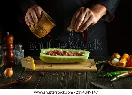 A professional chef in a black uniform adds salt to zucchini on the kitchen table. The idea of ​​preparing American national stuffed zucchini or mahshi for lunch.