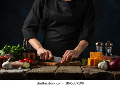 Professional chef in black uniform cuts with knife garlic on chopped wooden board. Backstage of cooking traditional mexican tacos on rustic wooden table. Close-up view. Dark blue background. - Powered by Shutterstock