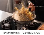 Professional chef cook making Italian Tagliatelle pasta with mushrooms and cream at kitchen gas stove in wok pan. Flying pasta levitation in motion.
