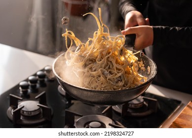 Professional chef cook making Italian Tagliatelle pasta with mushrooms and cream at kitchen gas stove in wok pan. Flying pasta levitation in motion. - Powered by Shutterstock