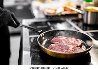 Professional chef cooking beef steak in frying pan on stove in restaurant kitchen - Powered by Shutterstock