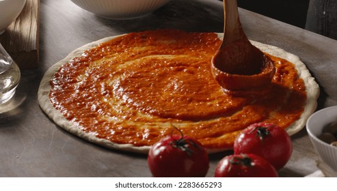 Professional chef is cooking pizza, spreading delicious tomato sauce on dough with a ladle. Cooker in restaurant kitchen. Food and drink close up  - Powered by Shutterstock