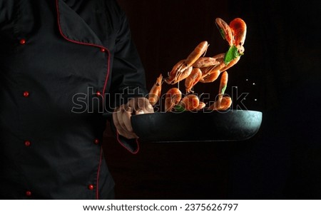 Professional chef cooks shrimp in a pan with parsley. Cooking seafood or healthy vegetarian food and meal on dark background. Freeze in motion. Free advertising space.