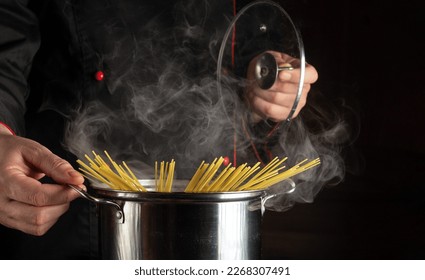 Professional chef cooks spaghetti in a pot with steam in the kitchen. Molecular cuisine. Free space for advertising on a black background