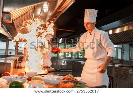 Professional chef creating flambé flame while cooking in a restaurant kitchen. Concept of high heat cooking, culinary performance, gastronomy technique and professional restaurant environment.
