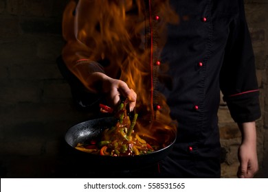 Professional chef and fire. Cooking vegetables and food over an open fire on a dark background. Hotel service photo background. Horizontal view.