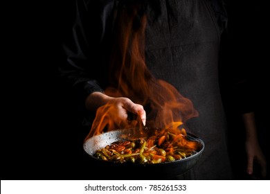 Professional chef and fire. Cooking vegetables and food over an open fire on a dark background. - Powered by Shutterstock