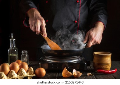 Professional Chef Frying Eggs In A Frying Pan. Cooking An Omelette With Egg In The Kitchen. Menu Or Recipe Idea For A Hotel.