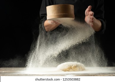 A professional chef in a professional kitchen prepares dough from flour to cook Italian pasta, pizza, the concept of nature, Italy, diet and biology. On a dark background. Design text placement