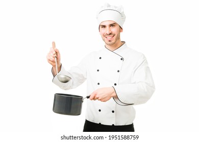 Professional Chef Making Eye Contact While Holding A Ladle And A Pot With Soup. Hispanic Worker Cooking A Soup At A Kitchen Restaurant