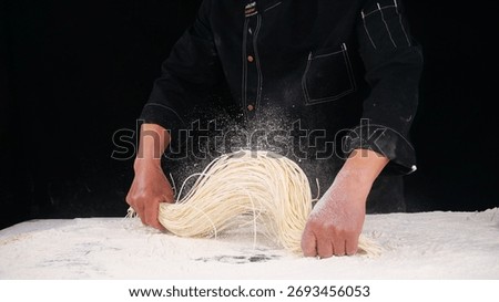 Professional chef making fresh handpulled noodles with flour dusting on dark background, showcasing traditional pasta making technique and culinary craftsmanship.