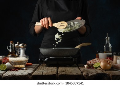 Professional Chef Pours Chopped Onion To Pan Wok. Backstage Of Cooking Traditional Indian Chicken Curry On Dark Blue Background. Concept Of Cooking Tasty Hot Meal.