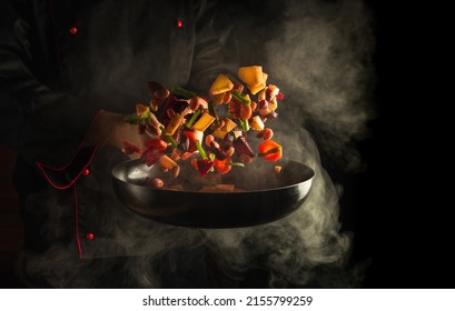 Professional chef prepares food in a hot pan with steam on a black background. The concept of restaurant and hotel service. Haute cuisine or Grande cuisine - Shutterstock ID 2155799259