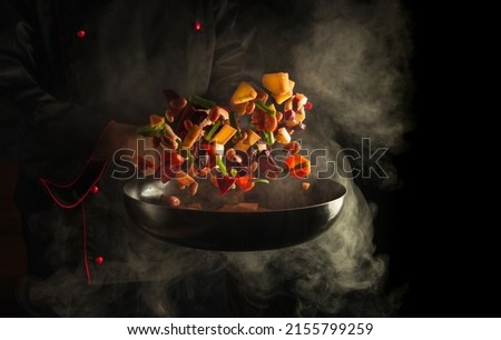 Professional chef prepares food in a hot pan with steam on a black background. The concept of restaurant and hotel service. Haute cuisine or Grande cuisine