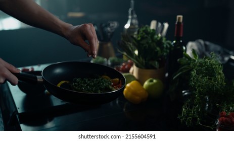 Professional Chef Seasoning Vegetables while Frying Them on a Hot Pan in a Dark and Industrial Looking Kitchen with a Colorful Background. - Powered by Shutterstock