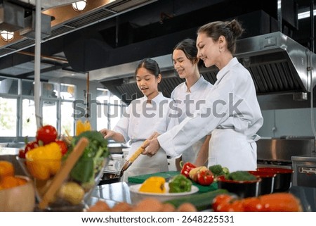 Professional chef is teaching young culinary class student to prepare fresh ingredient for the meal inside the restaurant kitchen for fine dining gourmet and cooking school