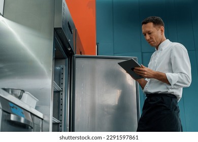 Professional chef using tablet computer recipes while working in modern kitchen cooking concept