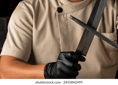 Professional chef wearing black gloves and sharpening knife for cook.Man in black latex gloves sharpens a knife at kitchen. - Powered by Shutterstock