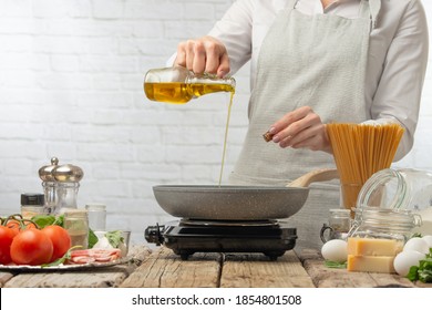 Professional chef in white uniform pours olive oil into frying pan for cooking pasta alla carbonara. Backstage of preparing traditional italian dish on white background. Frozen motion. Recipe book. - Powered by Shutterstock