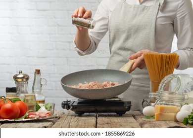 Professional chef in white uniform pours pepper on bacon in pan for cooking pasta alla carbonara. Backstage of preparing traditional italian dish on white background. Cooking process concept. - Powered by Shutterstock